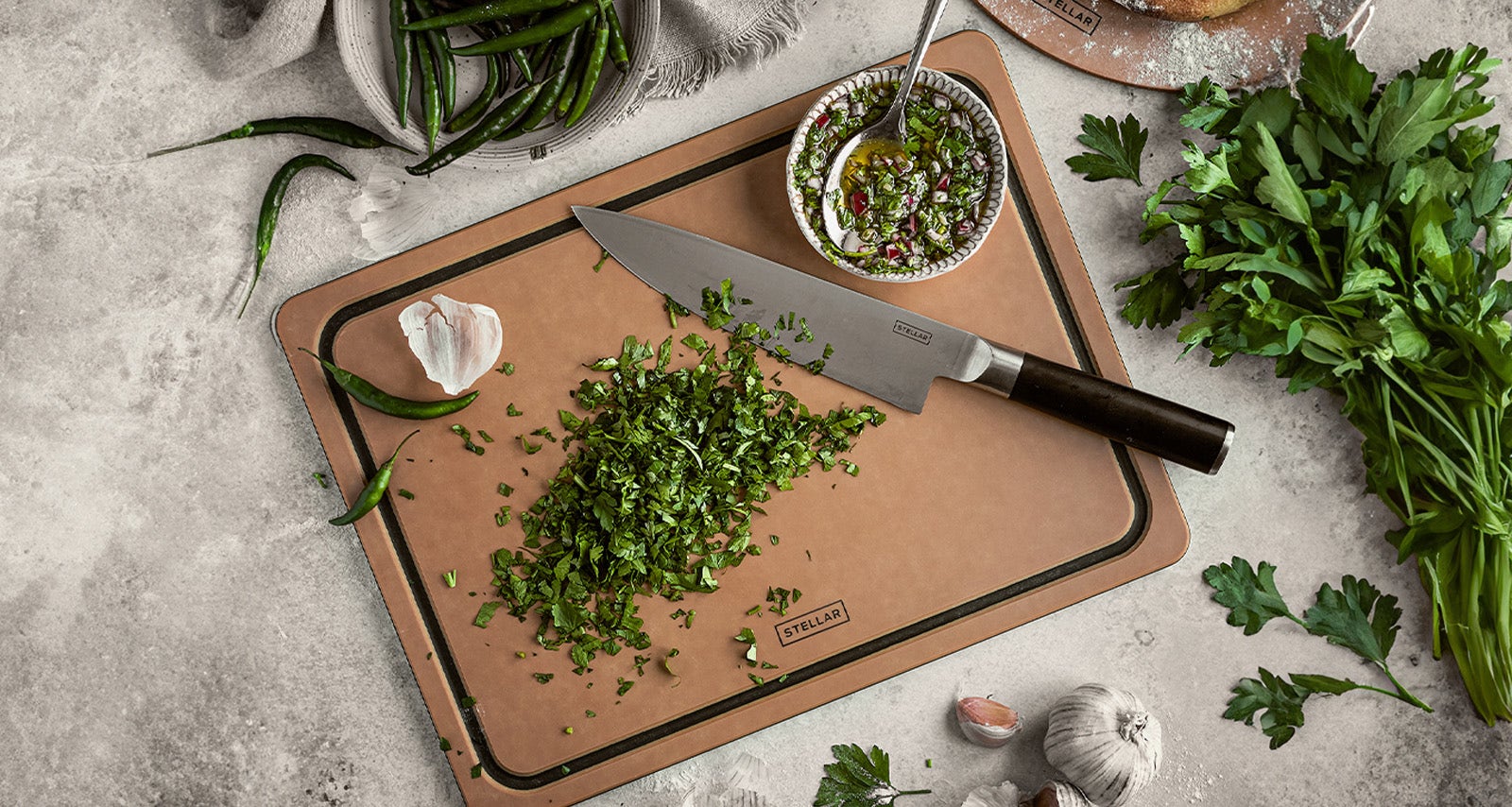 Stellar Form Chopping Board With Stellar Poise Knife Resting On Top With Chopped Herbs